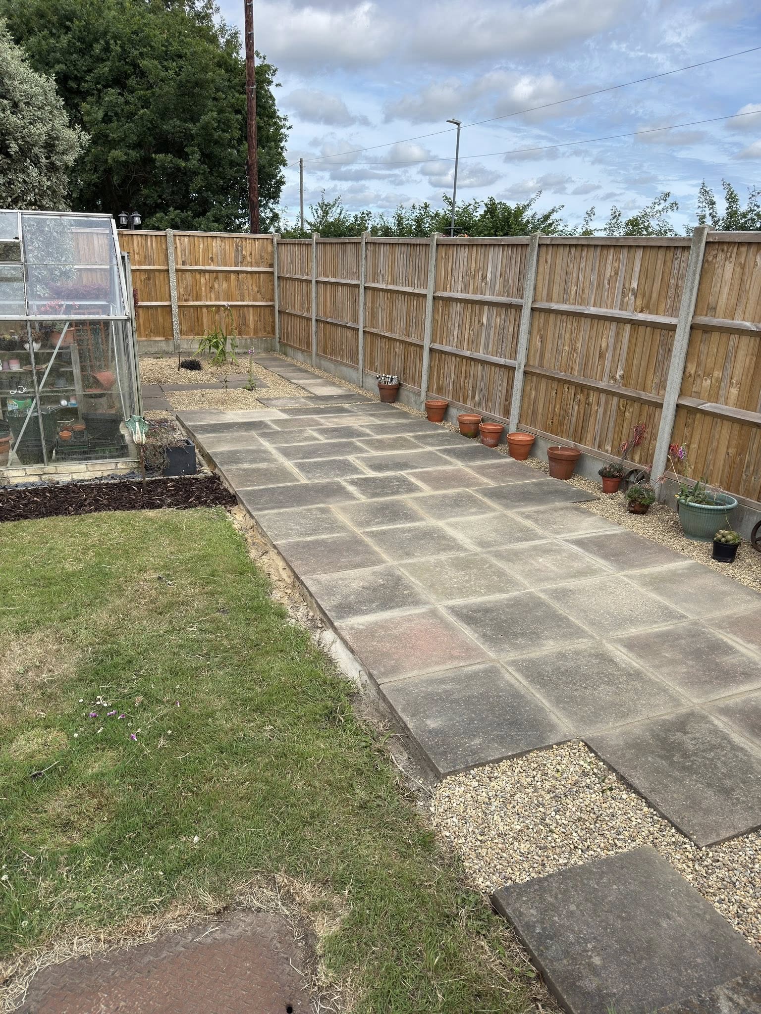 Patio slabs added to back garden with a glass greenhouse